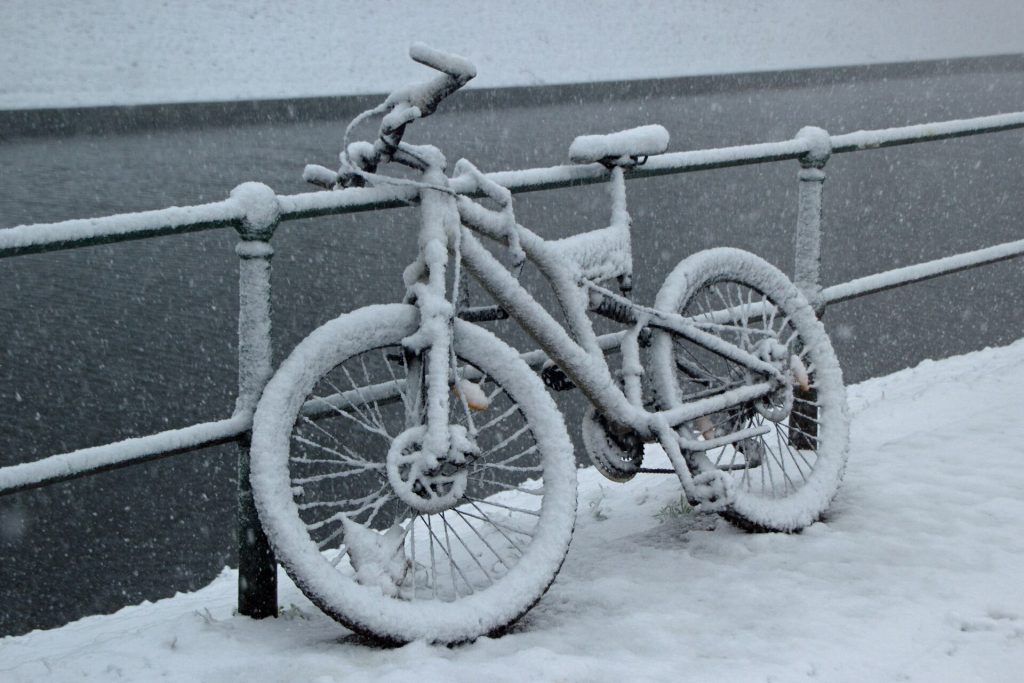 En snötäckt cykel lutad mot ett räcke vid en gata