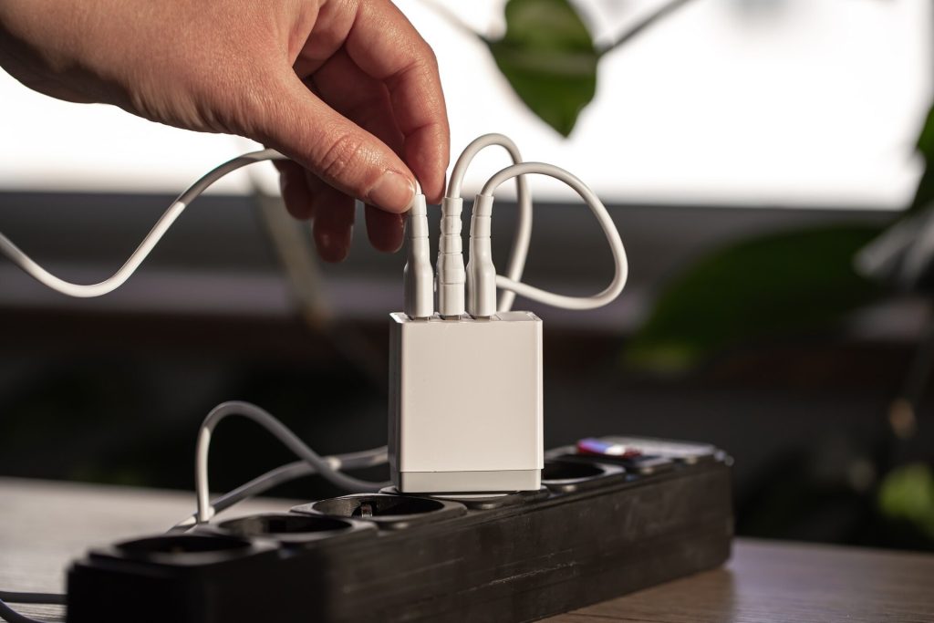 En hand kopplar kablar till en USB-laddare i ett grenuttag
